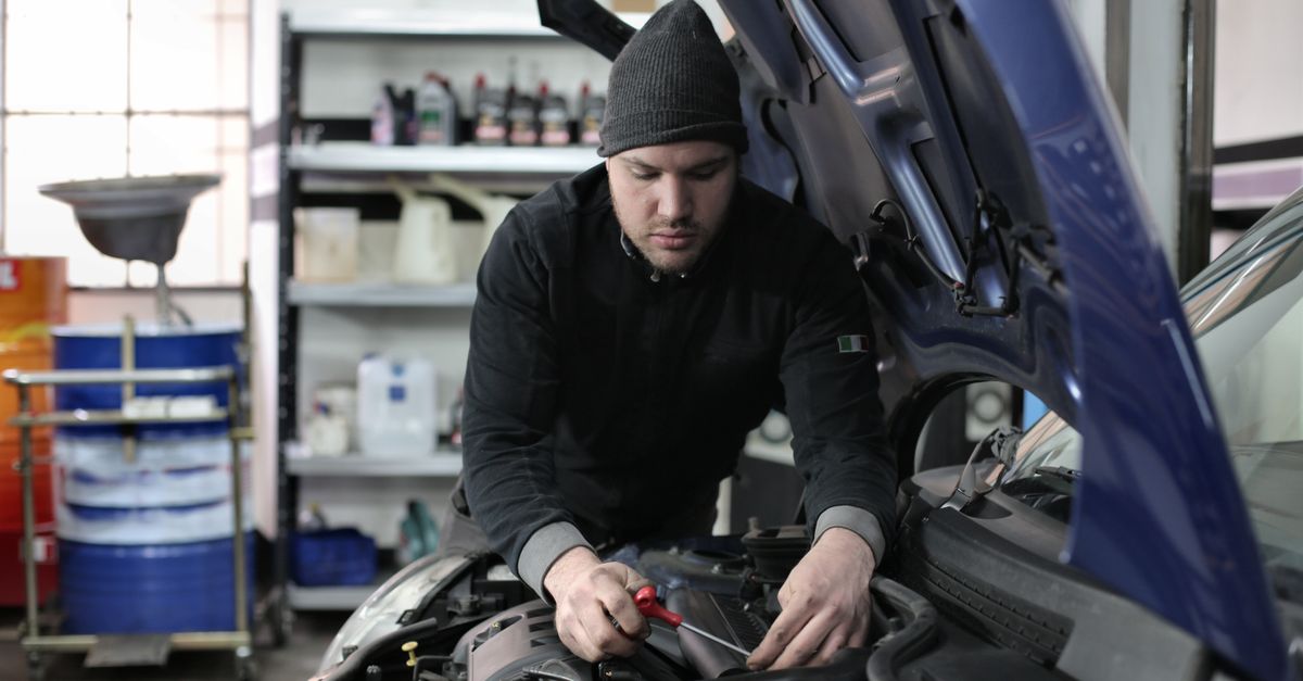mecánico trabajando bajo el capó de un auto en el taller